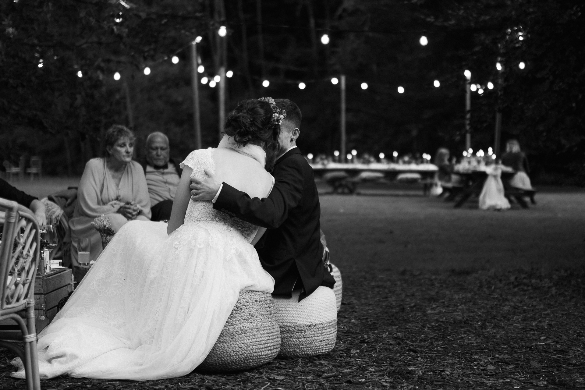 Brautpaar sitzt auf Heuballen und im Hintergrund ist die mit Lichterketten beleuchtete Hochzeotslocation zu sehen - Hochzeitsreportage Erkelenz