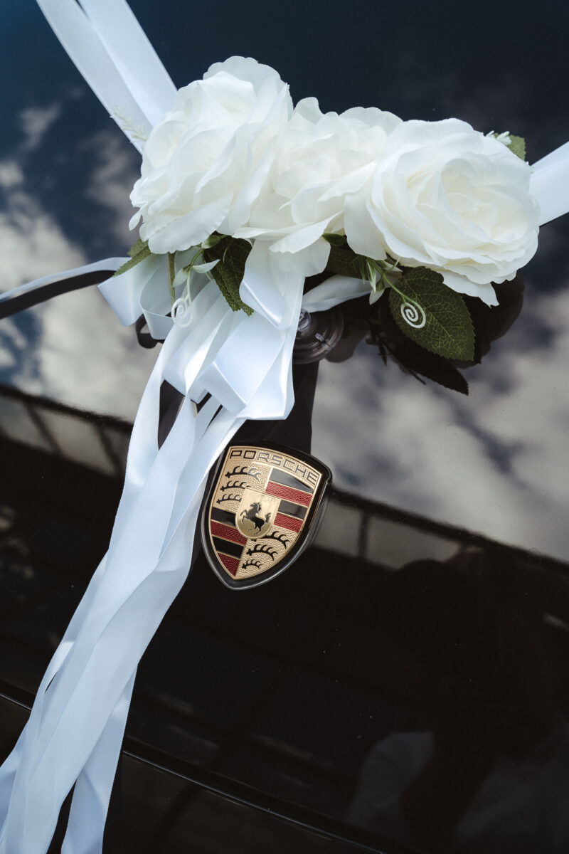 Hochzeitswagen geschmückt mit weißen Blumen und einer Schleife - Hochzeitsauto Porsche in Schwarz
