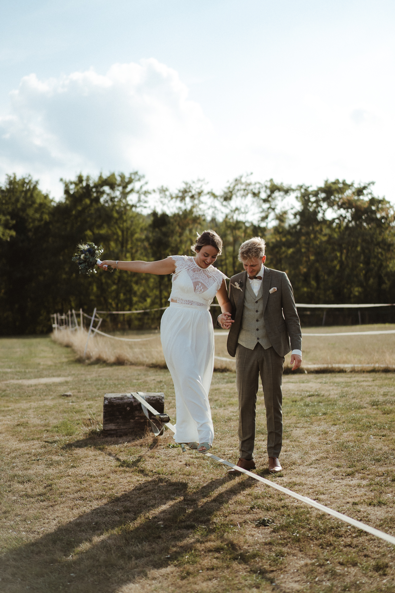 Braut balanciert über eine Leine. Ihr Bräutigam reicht ihr eine helfende Hand - natürliche Hochzeitsfotos Aachen