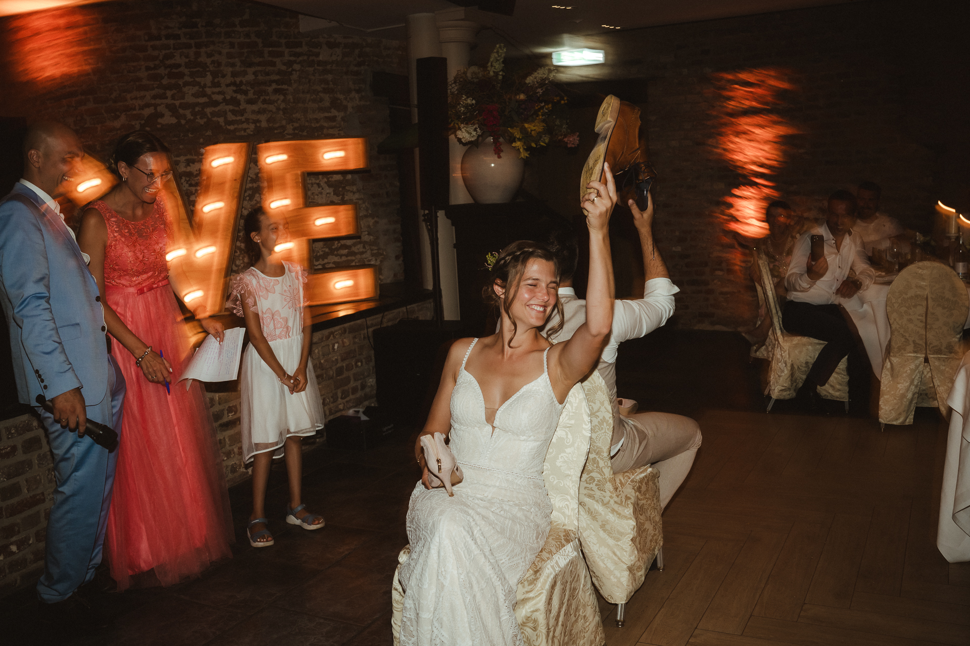 Brautpaar sitzt Rücken an Rücken und hält ihre Schuhe in die Luft - Braut lacht glücklich in die Kamera und hat die Augen leicht geschlossen - Hochzeitsfotos aus Aachen