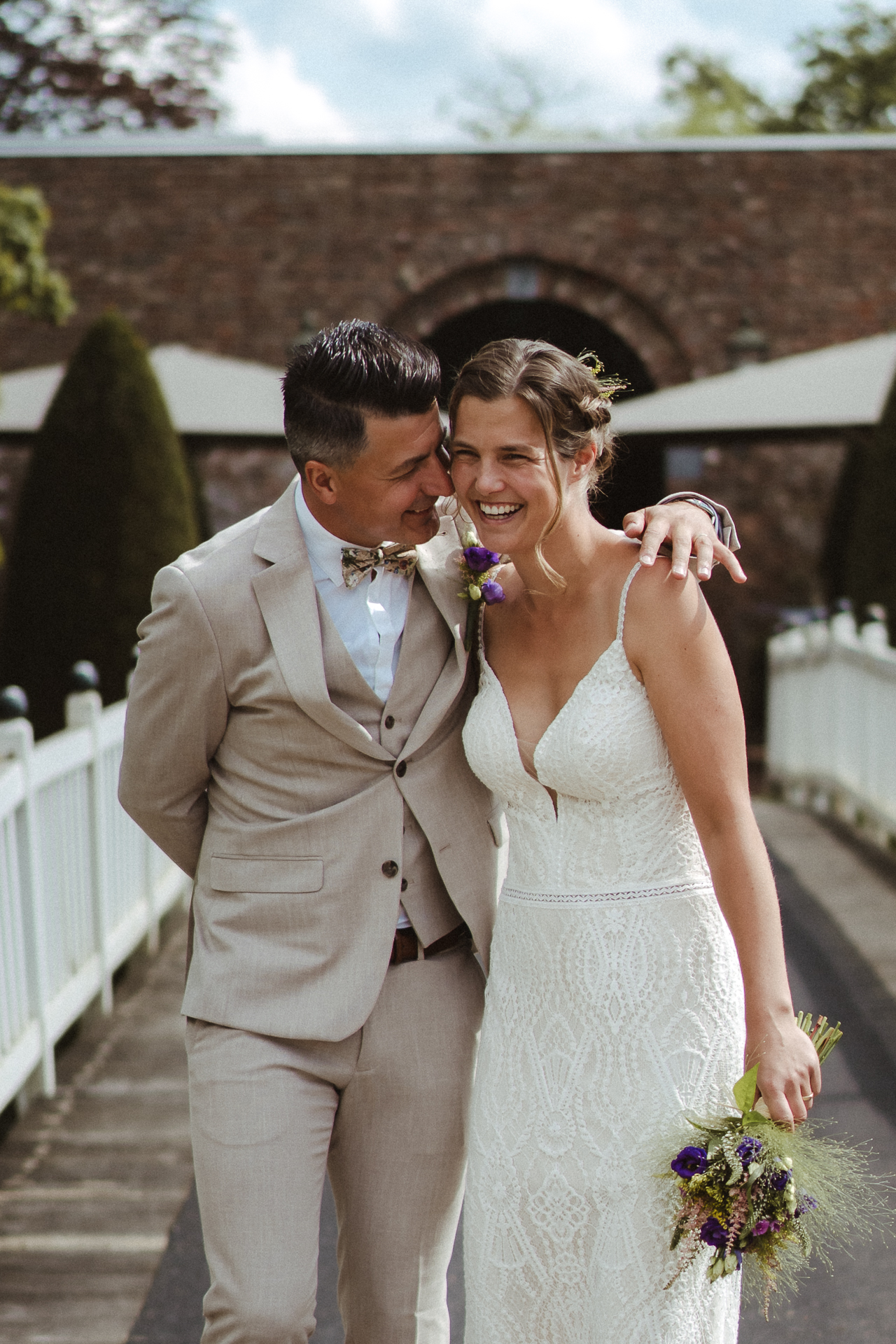 Brautpaar läuft über eine weiße Holzbrücke und lacht in die Kamera - wunderschöne Hochzeitsfotografie aus Düssseldorf
