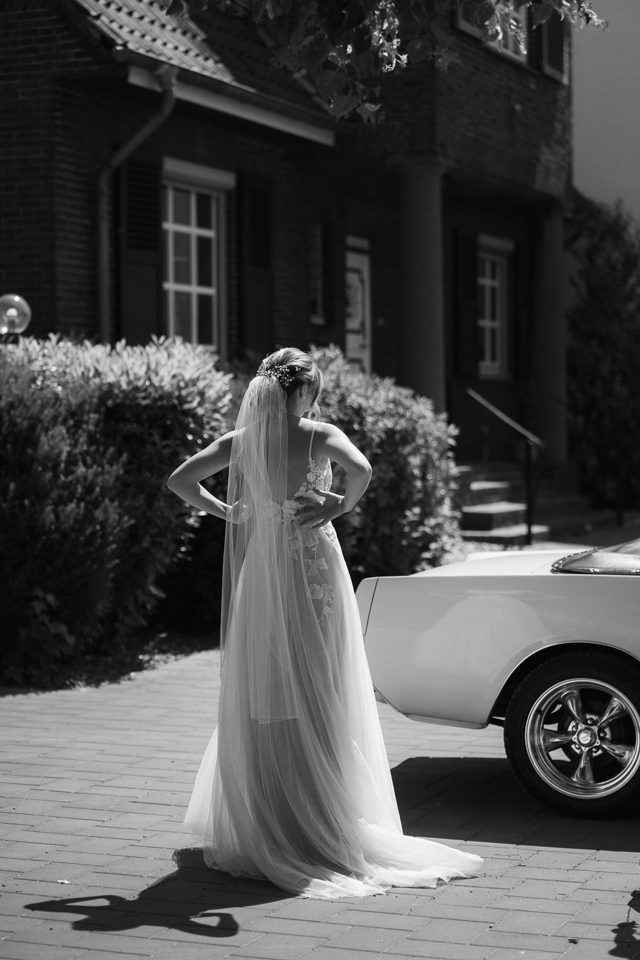 Braut steht vor ihrem Brautauto und richtet ihren Schleier - Paarshooting Erkelenz