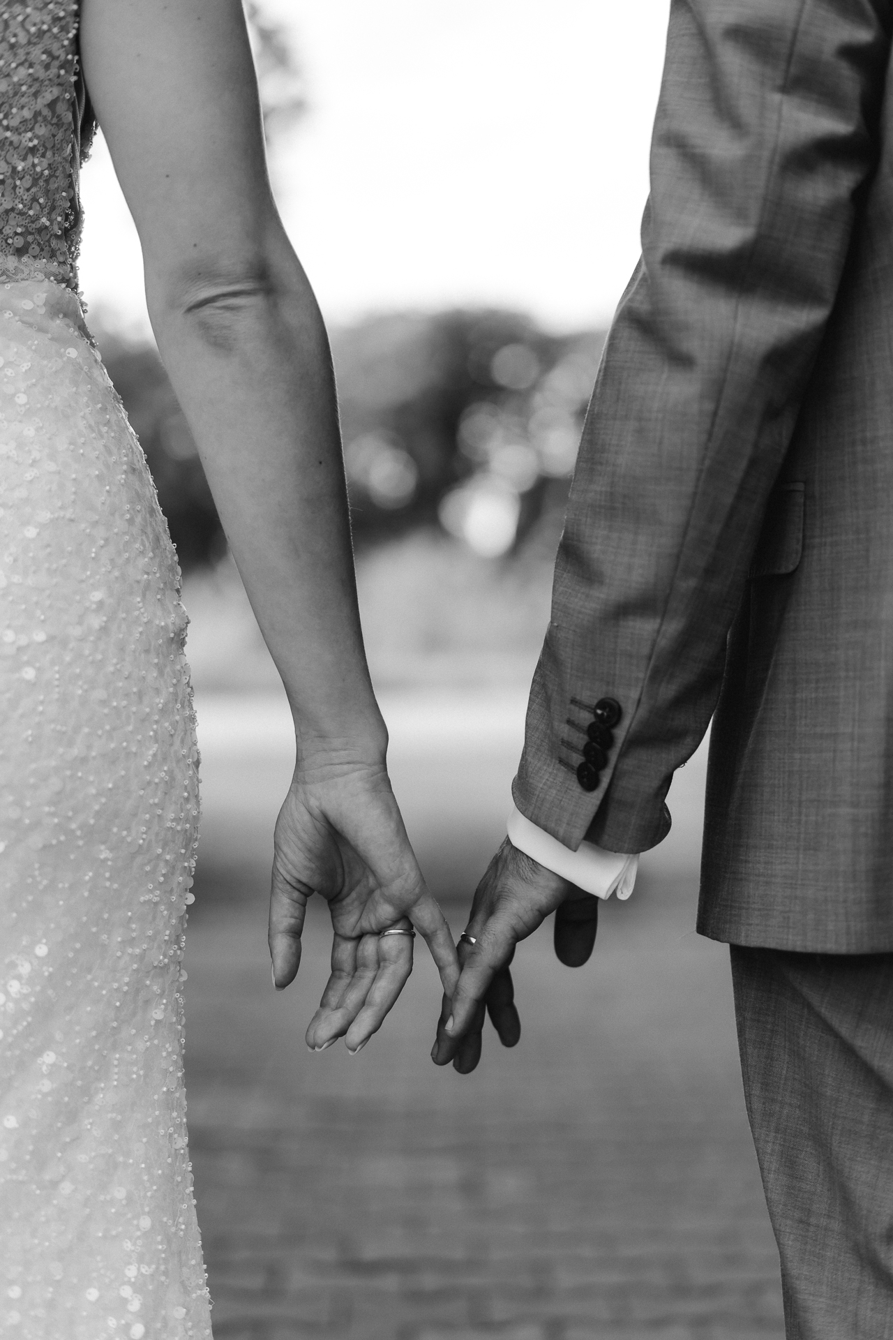 Die Hände eines Brautpaares berührend sich zärtlich am kleinen Finger. Der linke und rechte Bildrand wird von der Braut und Bräutigam begrenzt und die Hände sind im Zentrum des Bildes.