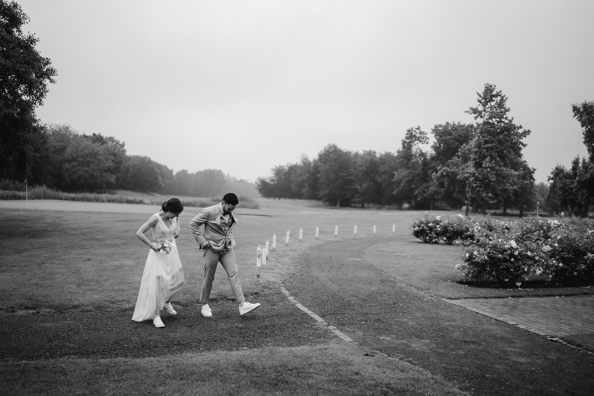 Brautpaar läuft über einen Golfplatz und zieht sich lustig die Hose und Kleid hoch - natürliche Hochzeitsfotos Düsseldorf