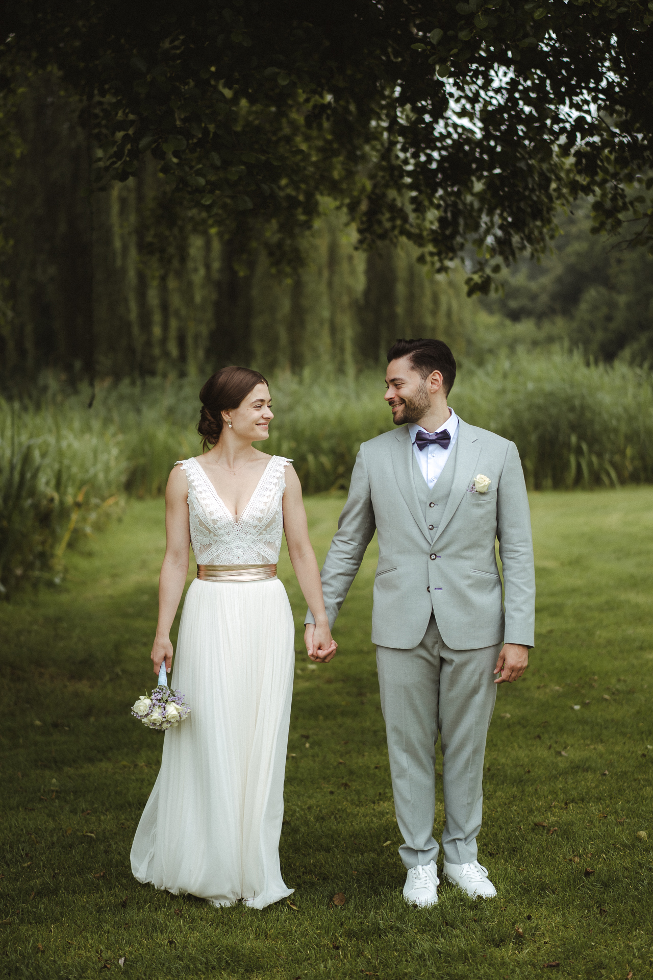 Brautpaar steht Hand in Hand und lächelt sich in der Mitte an - moderne Hochzeitsfotos Erkelenz