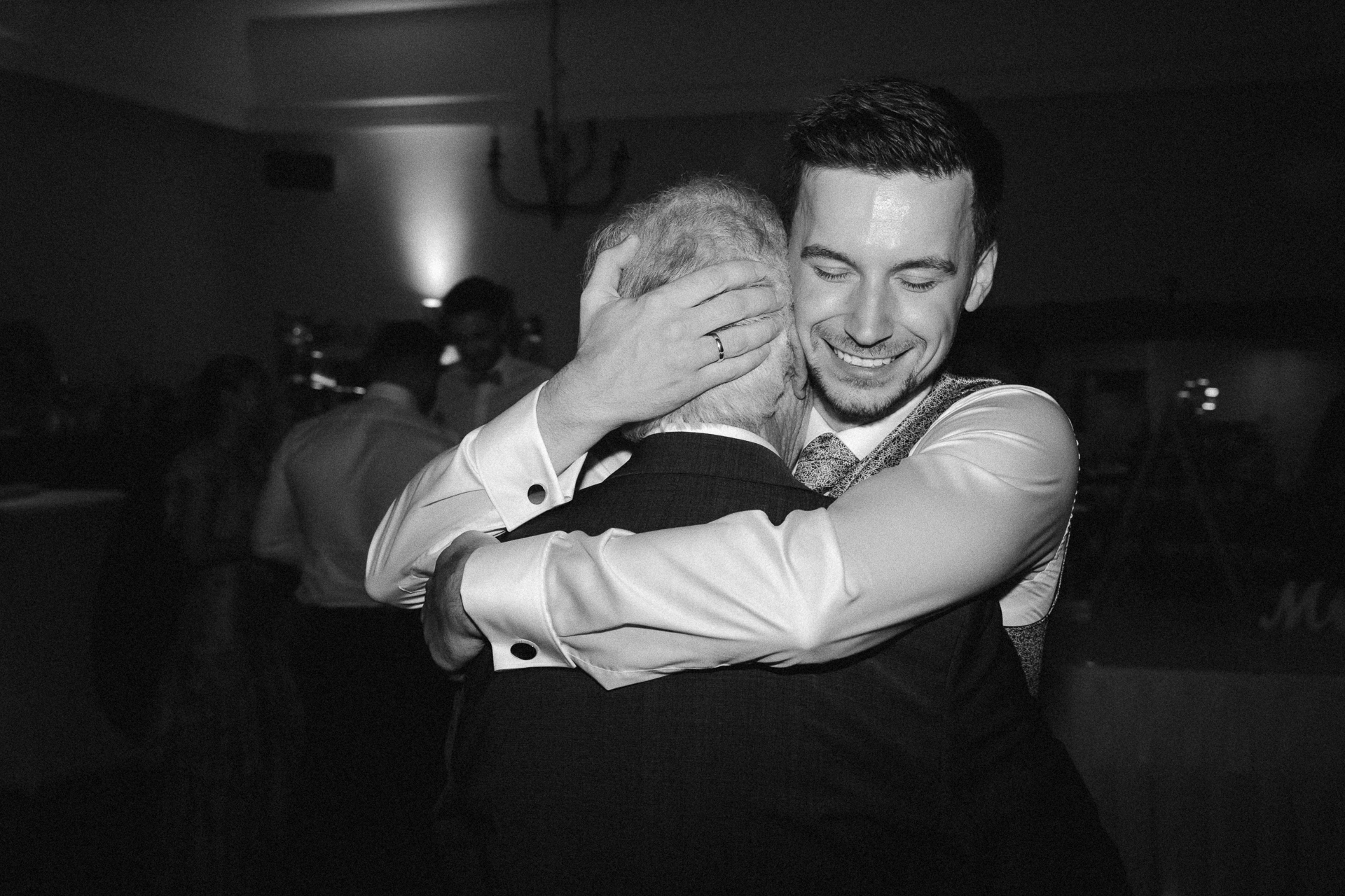 Bräutigam fällt seinem Opa auf der Hochzeit um den Arm und lacht verliebt in die Kamera - emotionale Familienfotos auf einer Hochzeit in Erkelenz