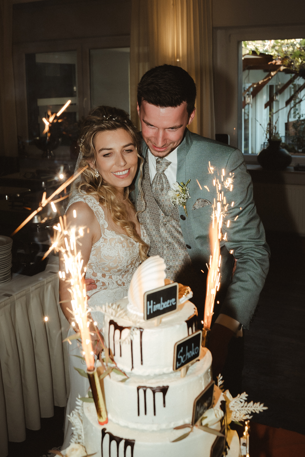 Brautpaar steht arm in arm vor einer Hochzeitstorte mit Tischfeuerwerk - Hochzeitsfeier in Erkelenz