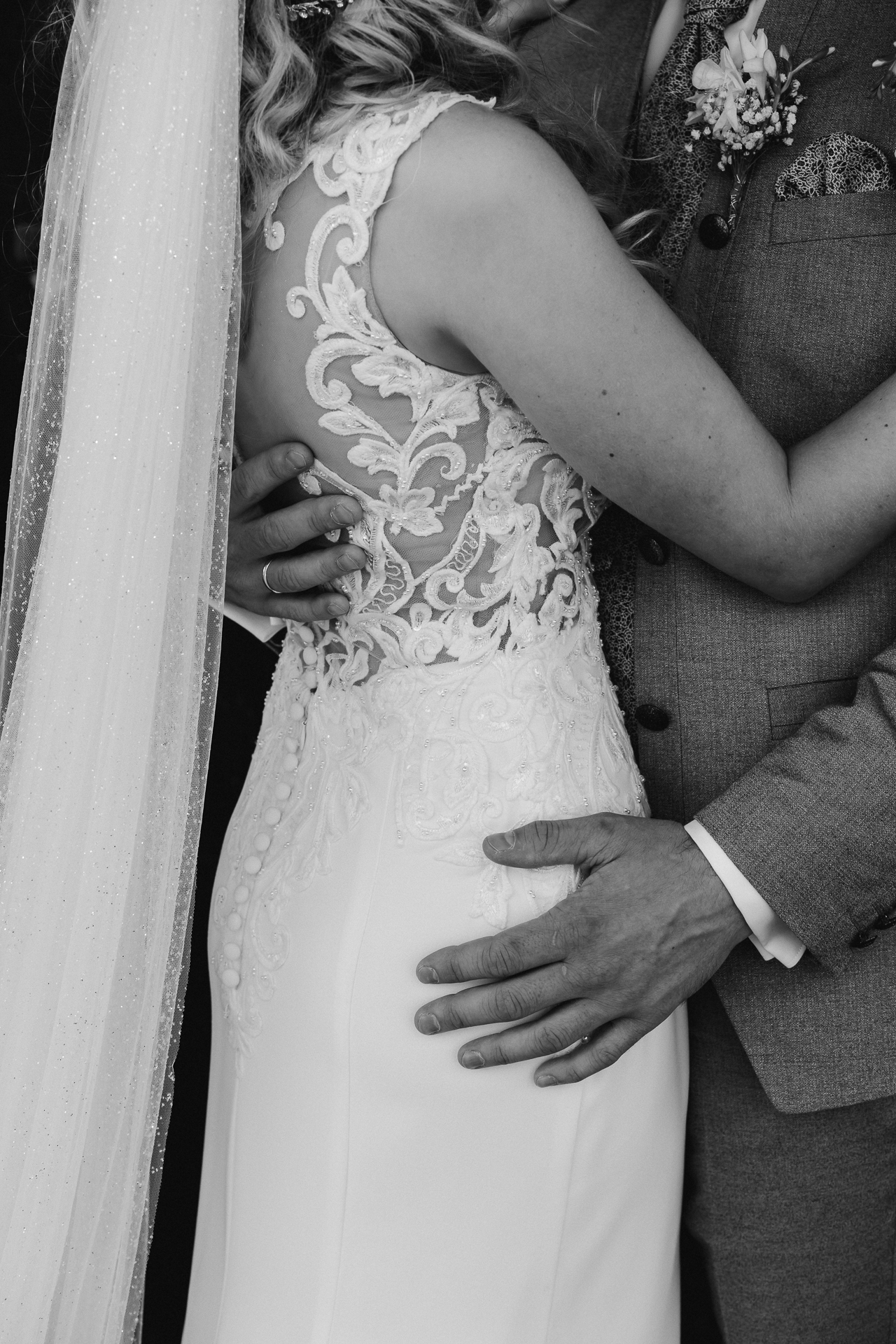 Detailfoto vom Brautkleid mit Spitze mit Blick auf den Rücken und Schleier der Braut. Die Hand des Bräutigam gleitet über die Hüfte - Hochzeitsfotograf Düsseldorf