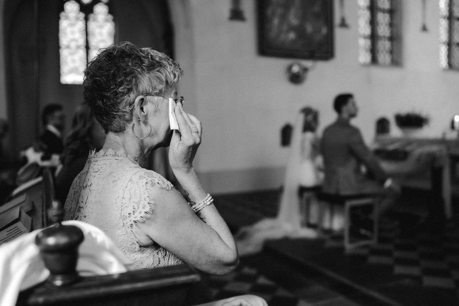 Frau im Abendkleid wischt sich eine Träne aus dem Gesicht während der kirchlichen Trauung - emotionaler Hochzeitsmoment