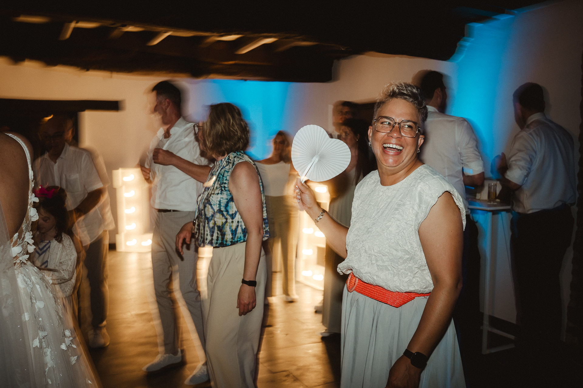 Partyfoto auf einer Hochzeit - Mutter der Braut tanzt, lacht und wedelt sich mit einem Herz Luft zu - Hochzeitsfotografie in Aachen